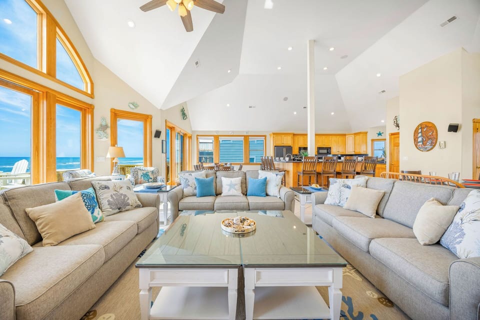 Settle into this bright, airy living space where vaulted ceilings and floor-to-ceiling windows frame stunning ocean views. Plush seating invites you to relax, while the open layout flows seamlessly into your fully-equipped kitchen.