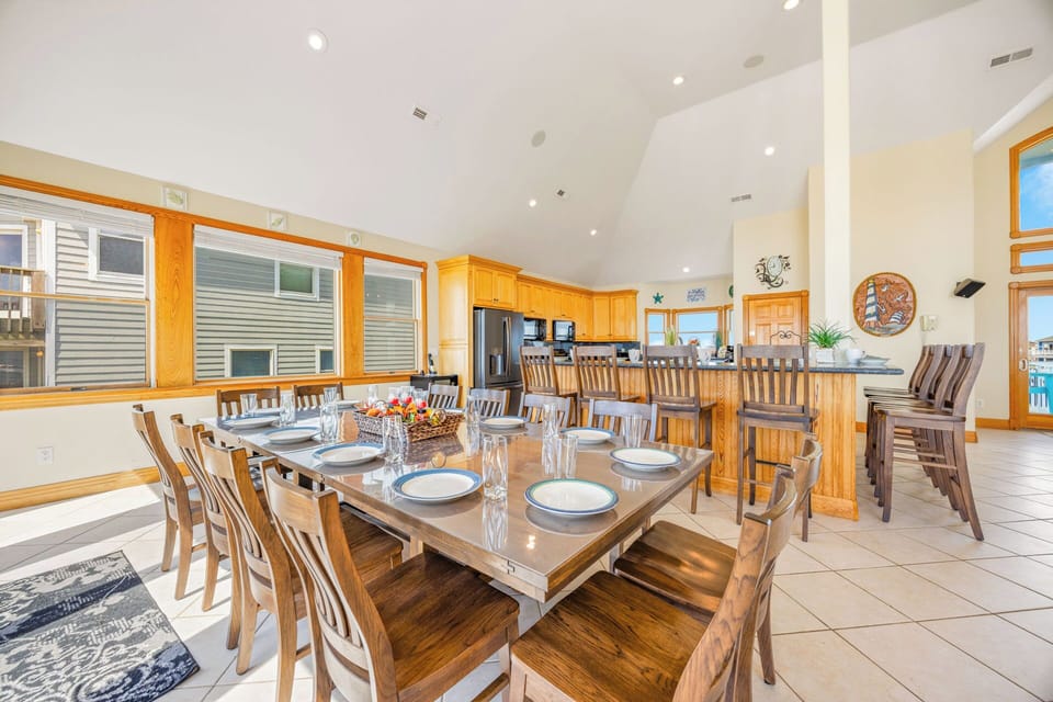 Gather around this spacious dining table set for memorable meals with your group. Natural light fills the open layout, connecting you to the full kitchen and bar seating—perfect for shared moments.