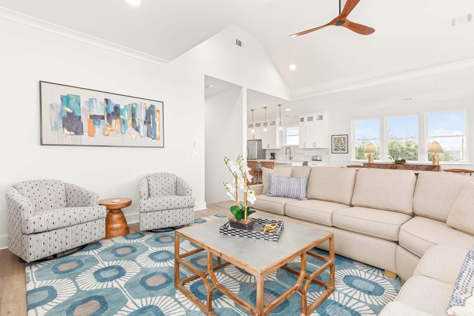 The open living room with a large sectional, flat-screen TV, and balcony access