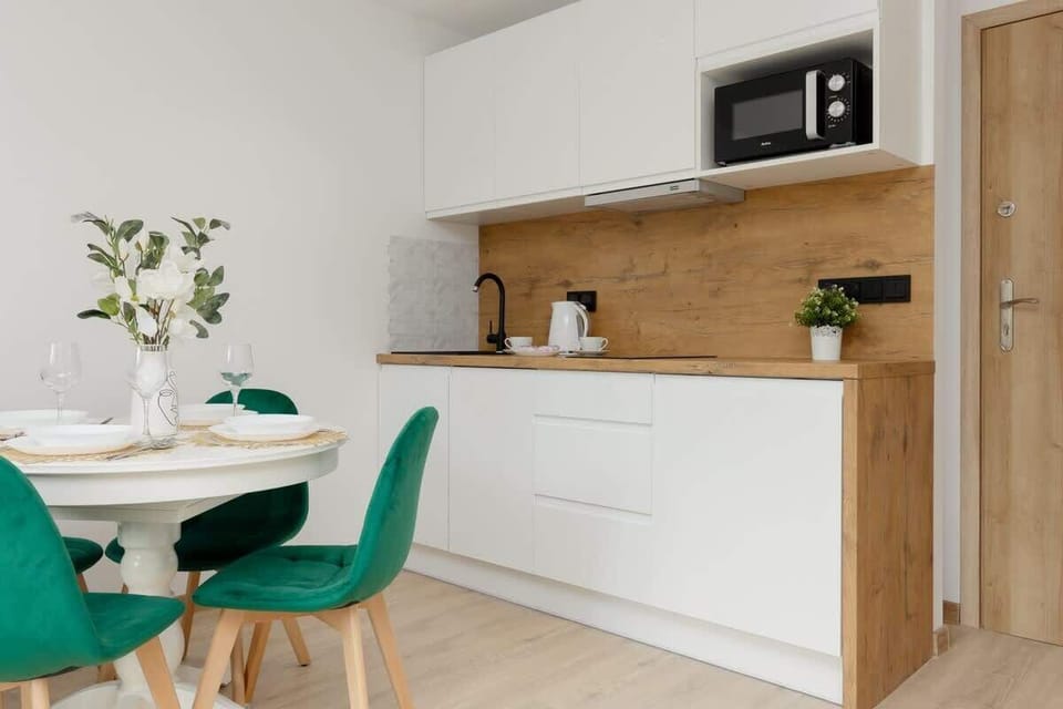 A modern kitchenette in white and wood tones, featuring a built-in microwave and sleek design.
