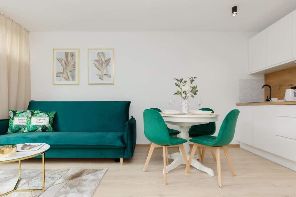 A wider view of the living space, combining a teal sofa, a dining area with green chairs, and minimalist decor.

