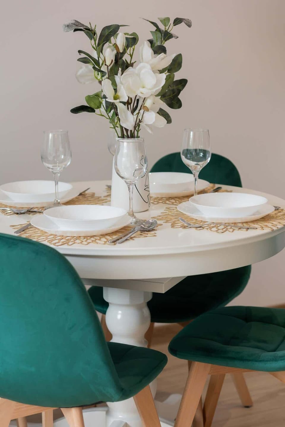 A cozy dining area with green upholstered chairs, a round table, and a vase of fresh flowers.
