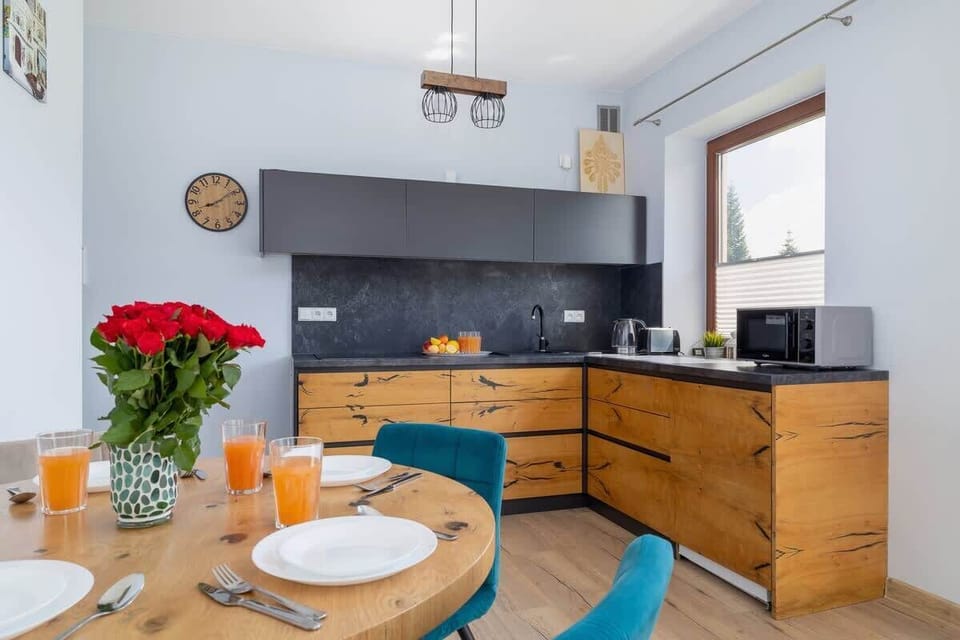 A stylish open-concept kitchen and dining corner with wooden cabinets, red flowers, and fresh juice adding a welcoming touch.
