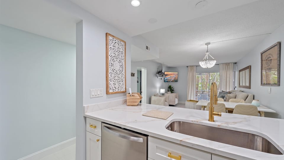 A kitchen with a large marble countertop and a gold faucet, with an open view of the living and dining areas.