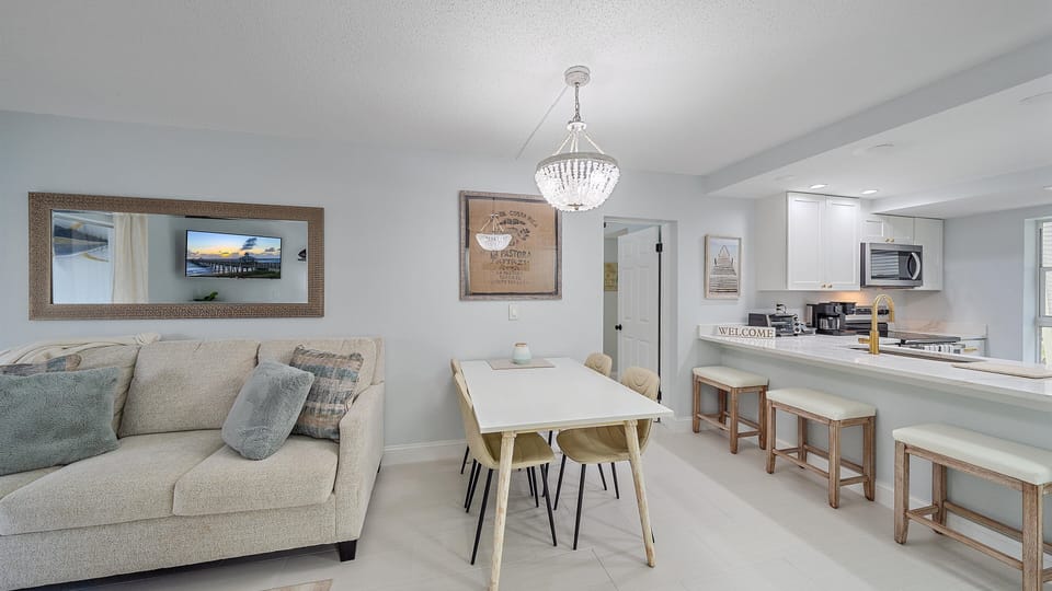 A living room and kitchen with an open floor plan, featuring a comfy sofa, a dining table, and a kitchen bar.