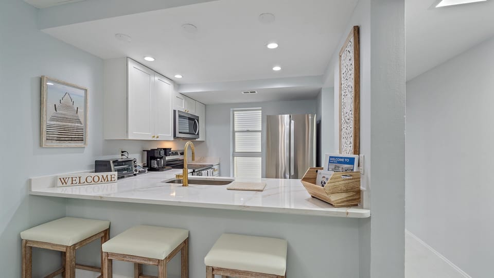 A clean kitchen with white cabinets, a large marble countertop, and a breakfast bar with three stools.
