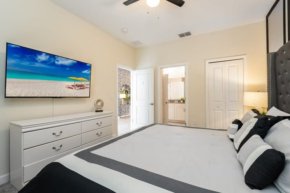 Bedroom with a plush tufted headboard, crisp white bedding, and a wall-mounted TV featuring a turquoise tropical beach scene.