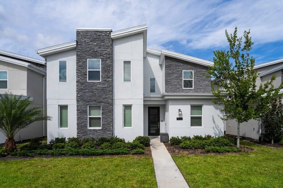 Modern villa exterior with a dramatic stacked-stone facade, landscaped lawn, and a welcoming walkway leading to the private entrance.