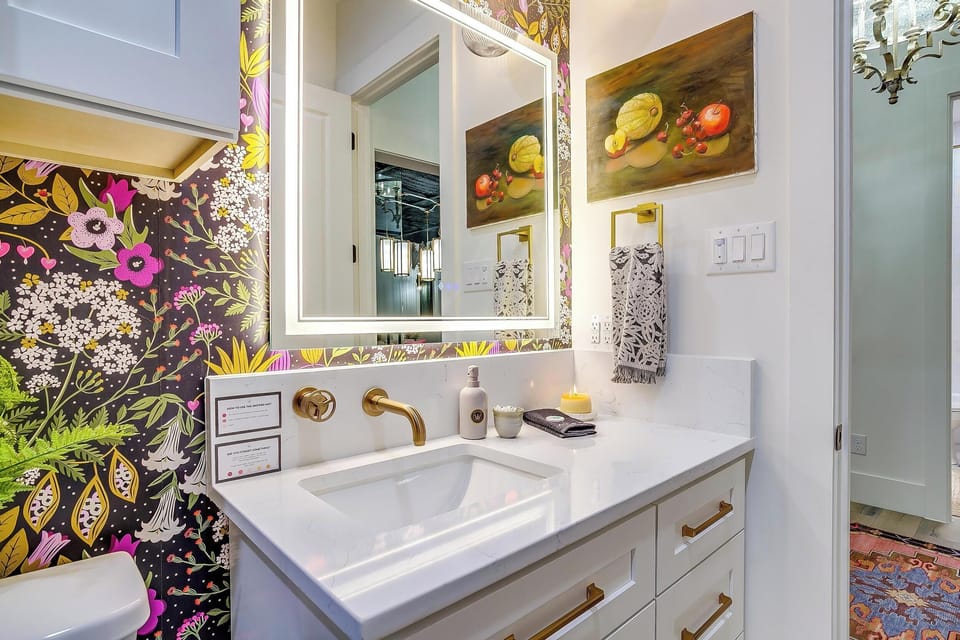 Bold floral wallpaper, gold fixtures, lit vanity mirror. The bathrooms at The Noir don't apologize for anything. 