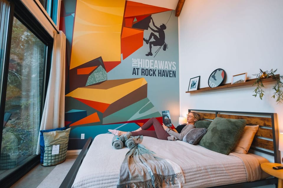 Main-level bedroom with a queen bed and Serta Stay Cool pillows. Big windows and a bold climbing mural make it easy to sink in after a day on the trails.