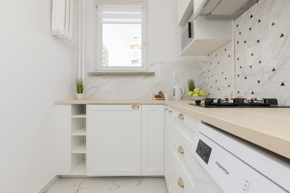 A white kitchen with a patterned backsplash, generous counter space, and natural light streaming in from a nearby window, creating a cheerful cooking area.
