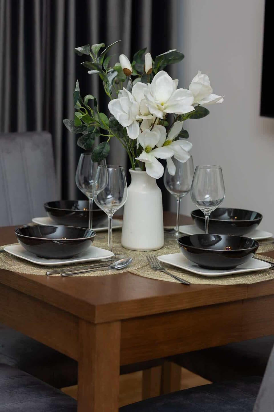 A wooden dining table set with elegant tableware and a vase of fresh flowers, creating a welcoming atmosphere.

