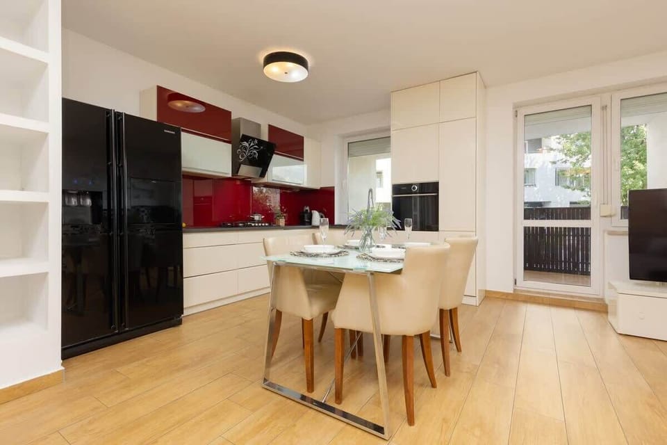 A wider perspective of the kitchen and dining area, showing how the red backsplash adds energy to the clean, white cabinetry and furnishings.

