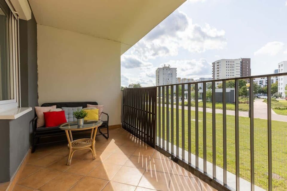 A balcony with wooden flooring, outdoor furniture, and views of a green residential area, perfect for relaxation.

