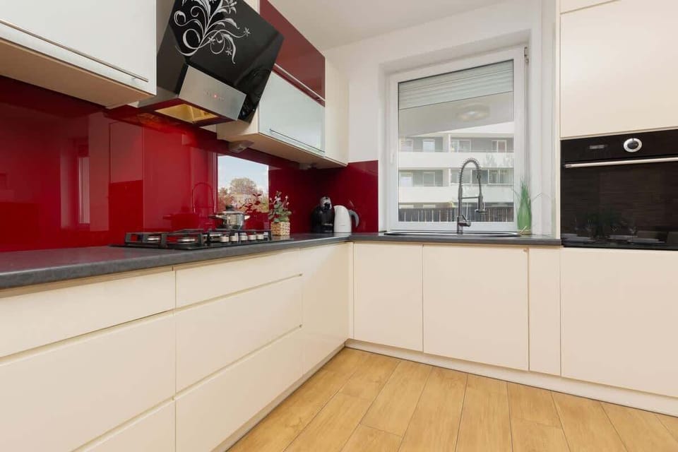 A sleek kitchen with white cabinets, a bold red backsplash, and modern appliances, offering a stylish and vibrant design.

