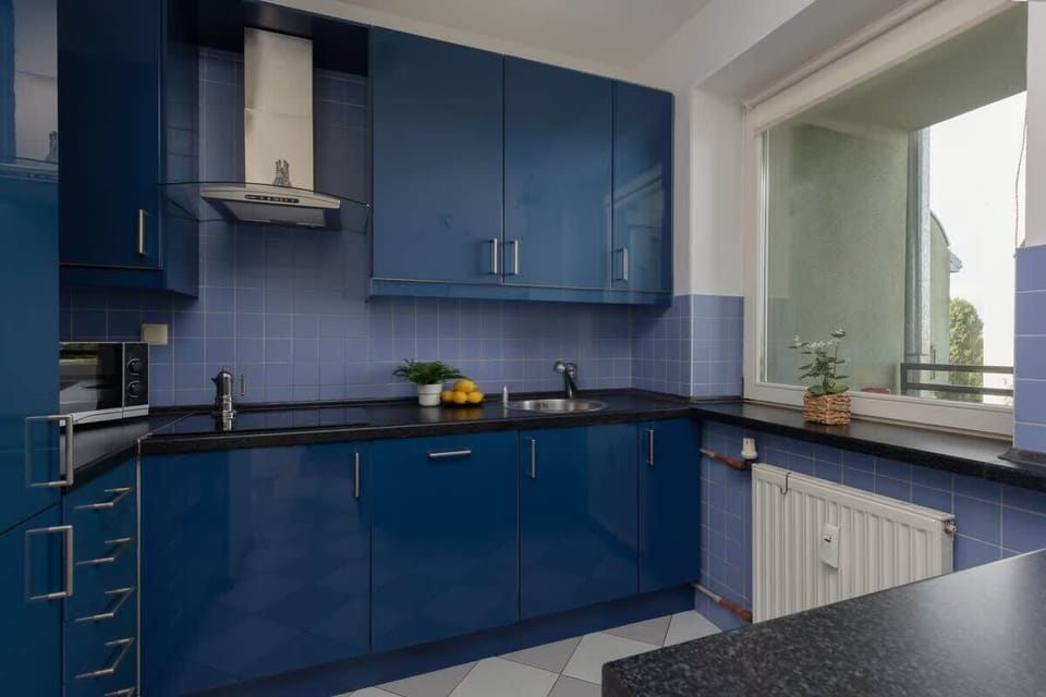 A modern kitchen with deep blue cabinets, a granite countertop, and a bright window providing plenty of natural light.

