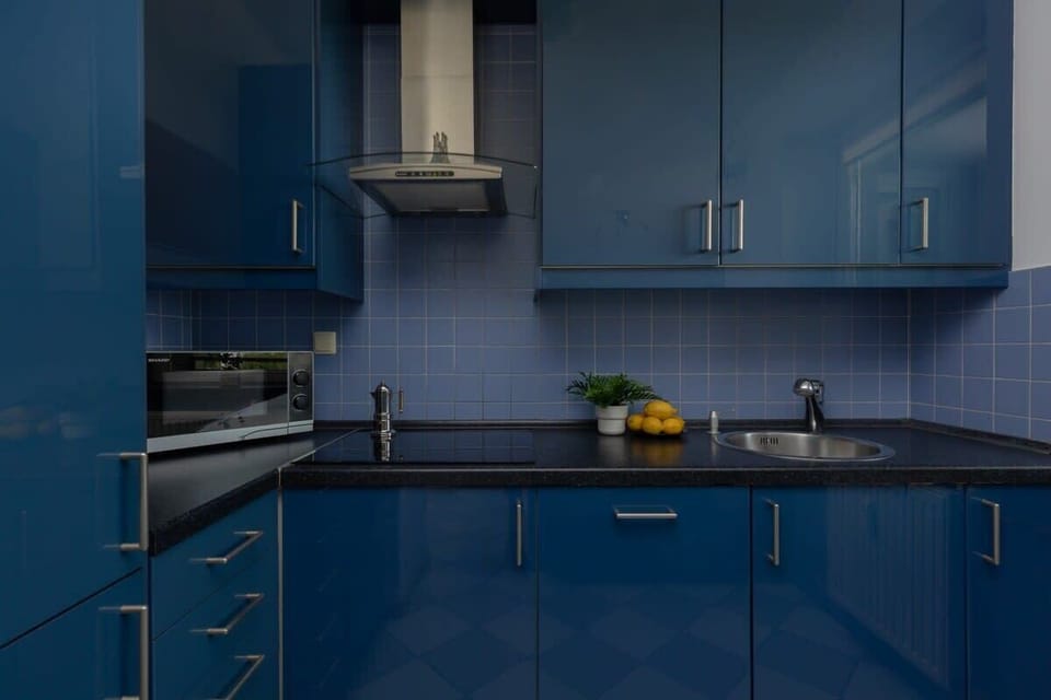 A closer perspective of the kitchen corner, emphasizing the glossy blue cabinetry, tiled backsplash, and built-in modern appliances.

