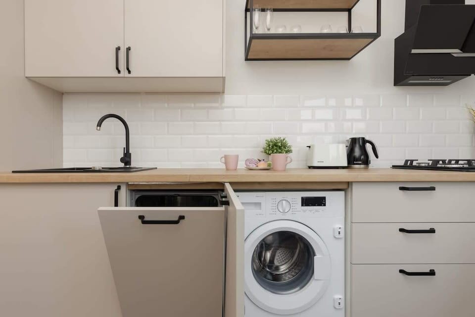 Another view of the kitchen, featuring integrated appliances, wooden accents, and a washing machine for added functionality.

