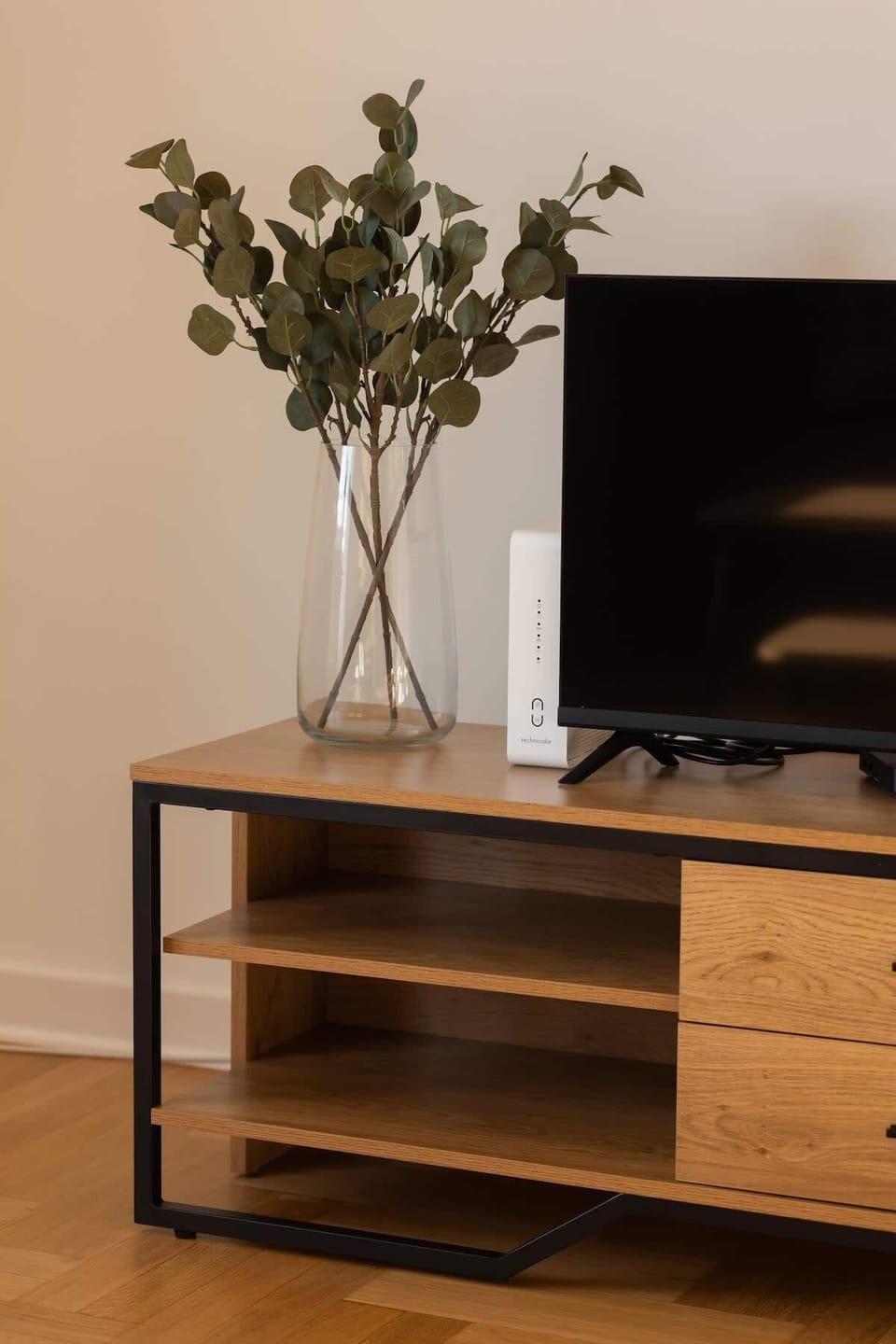 A wooden TV stand with a flat-screen TV, minimal decor, and potted plants, blending natural elements with a modern interior.

