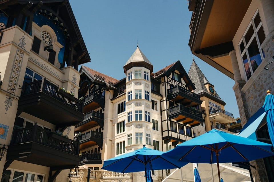 Tall alpine-style hotel with pointed turret towers above a terrace lined with blue umbrellas