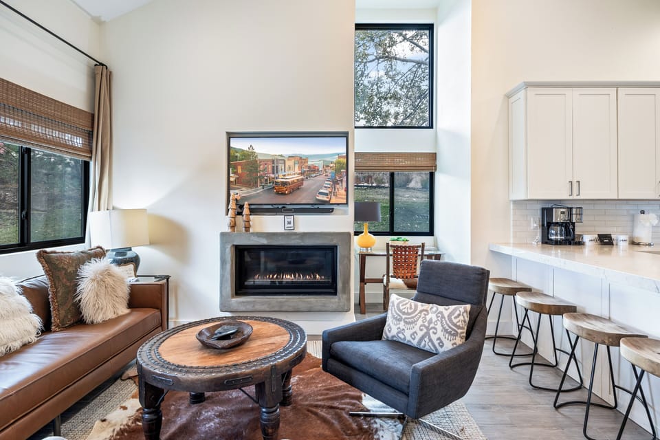 Warm and inviting living space featuring a sleek fireplace, high ceilings, and large windows that fill the room with natural light. Thoughtful design elements create the perfect spot to relax and unwind.
