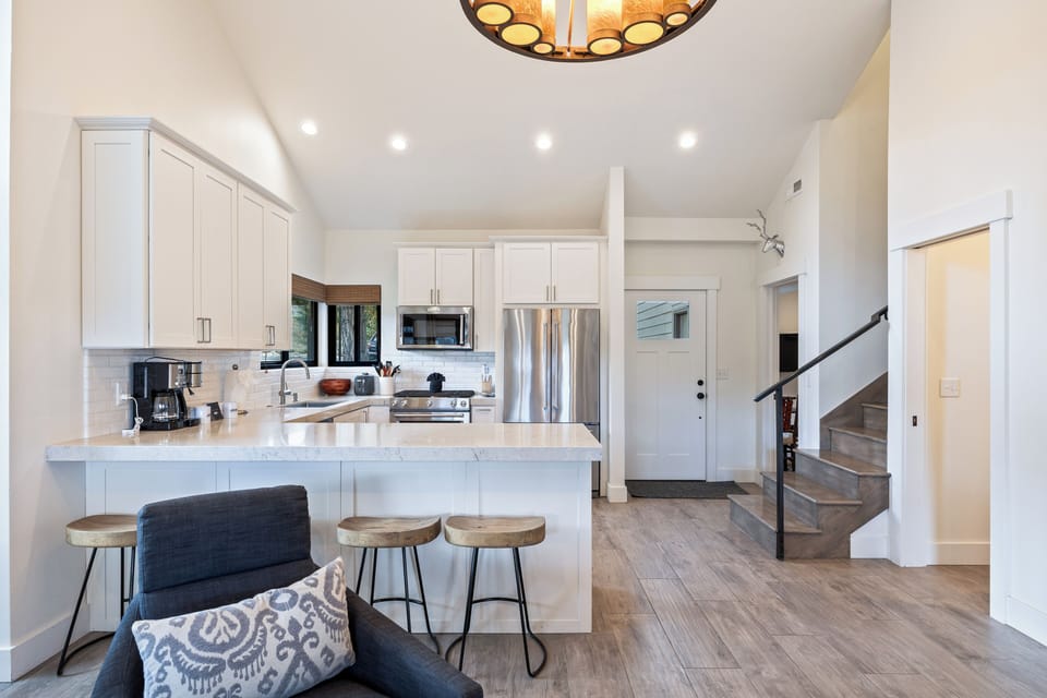 Bright, fully equipped kitchen with stainless steel appliances, quartz countertops, and a spacious breakfast bar with seating for three. Perfect for preparing meals and enjoying casual dining in a beautifully designed open-concept layout.