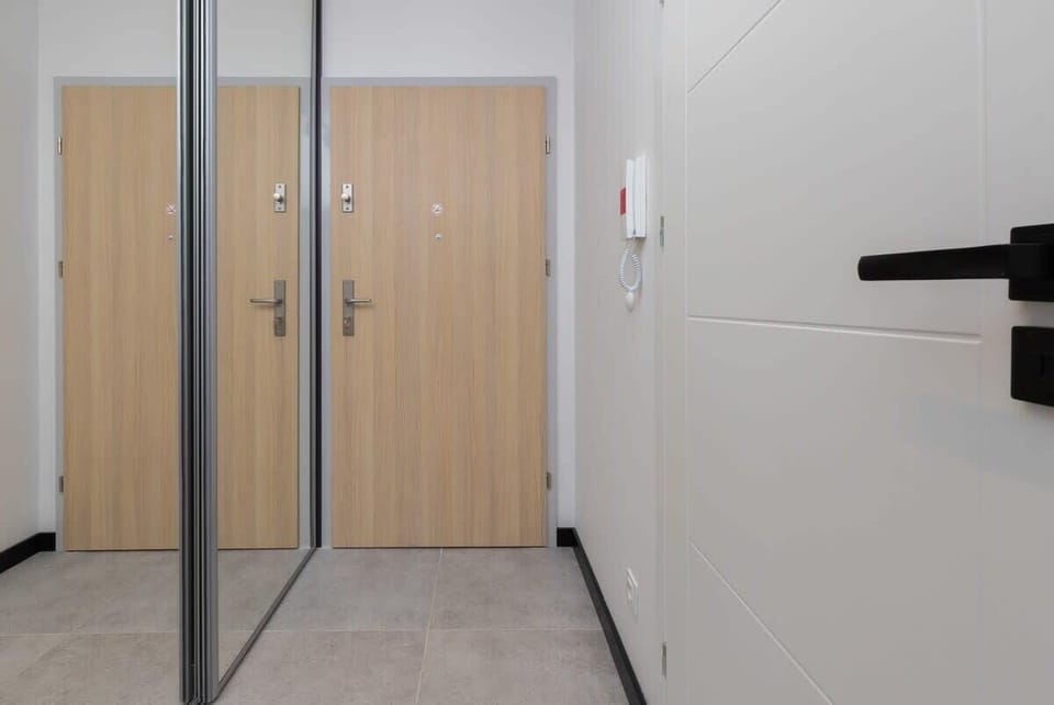 An entryway with a clean, minimalist design, featuring a wooden door, tiled floor, and sleek walls.

