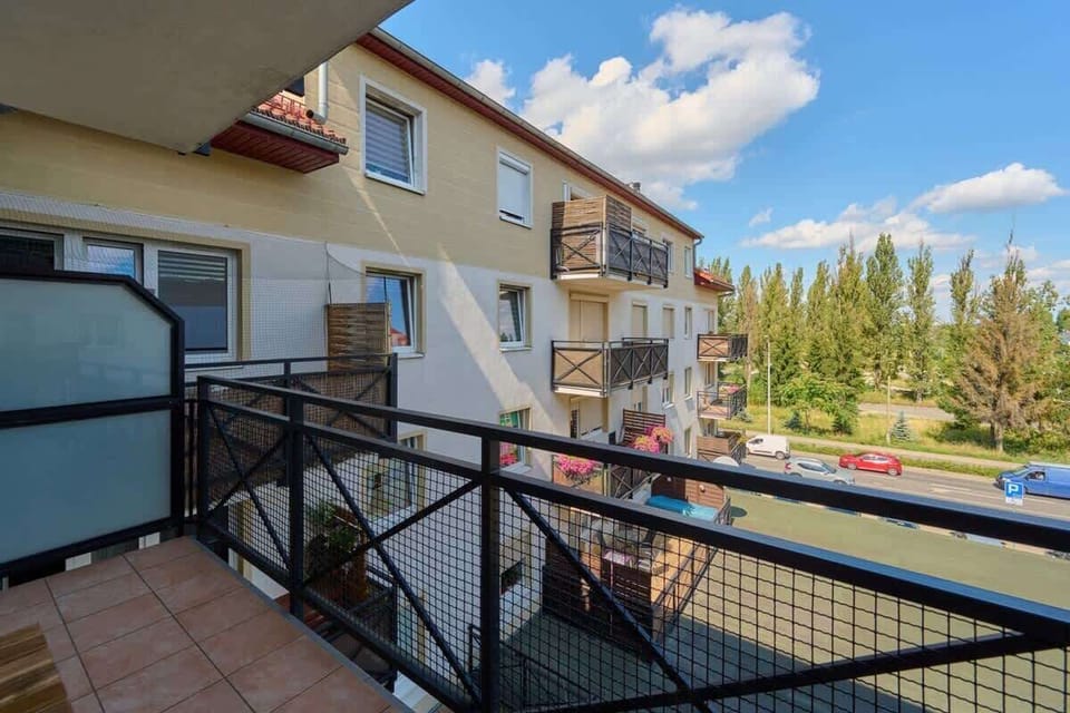 A balcony with a metal railing, offering an outdoor space with views of a quiet residential area and surrounding greenery.
