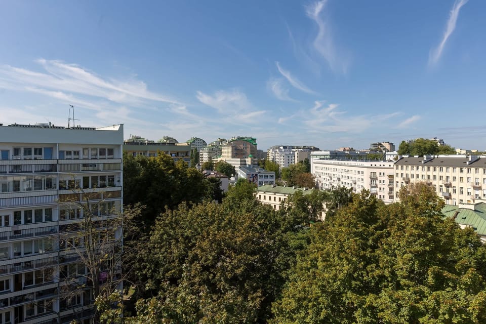 A panoramic view of the residential area from the balcony, surrounded by greenery and urban structures.

