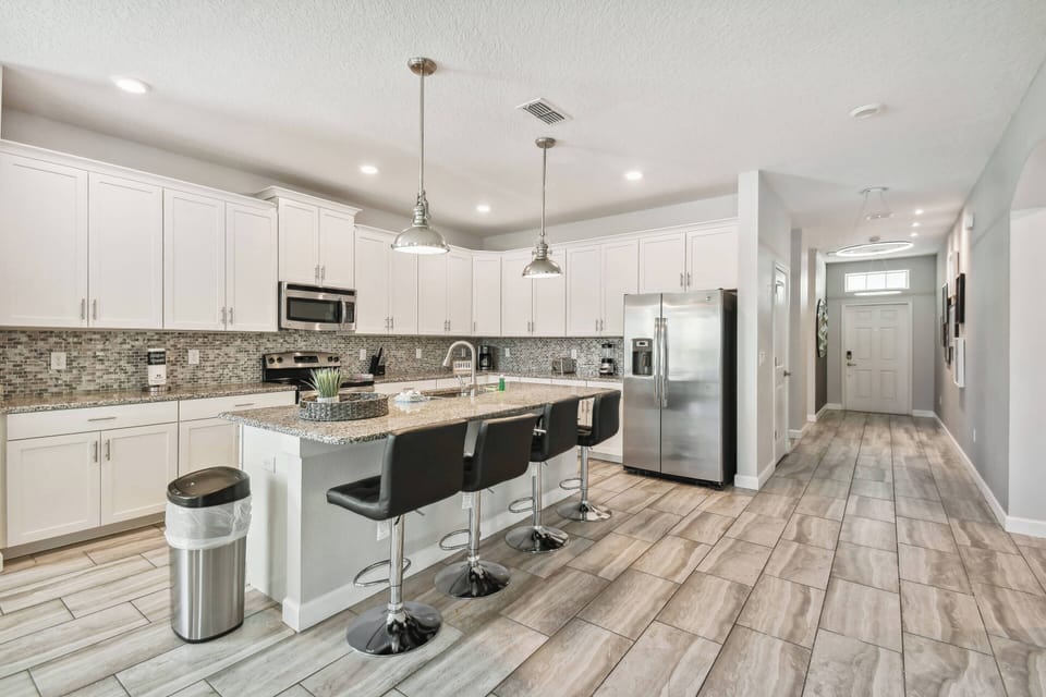 Enjoy the bright and inviting atmosphere of this spacious kitchen, featuring sleek white cabinetry and a stunning backsplash. The contemporary bar stools invite casual conversations, while the ample counter space enhances meal.