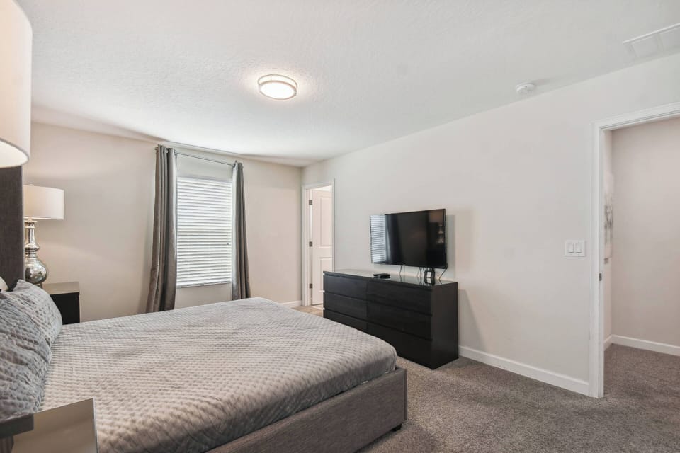 Relax in this cozy bedroom featuring a plush, inviting bed and soft gray carpet underfoot. The room is thoughtfully designed with sleek furniture and large windows that fill the space with natural light, enhancing your comfort.
