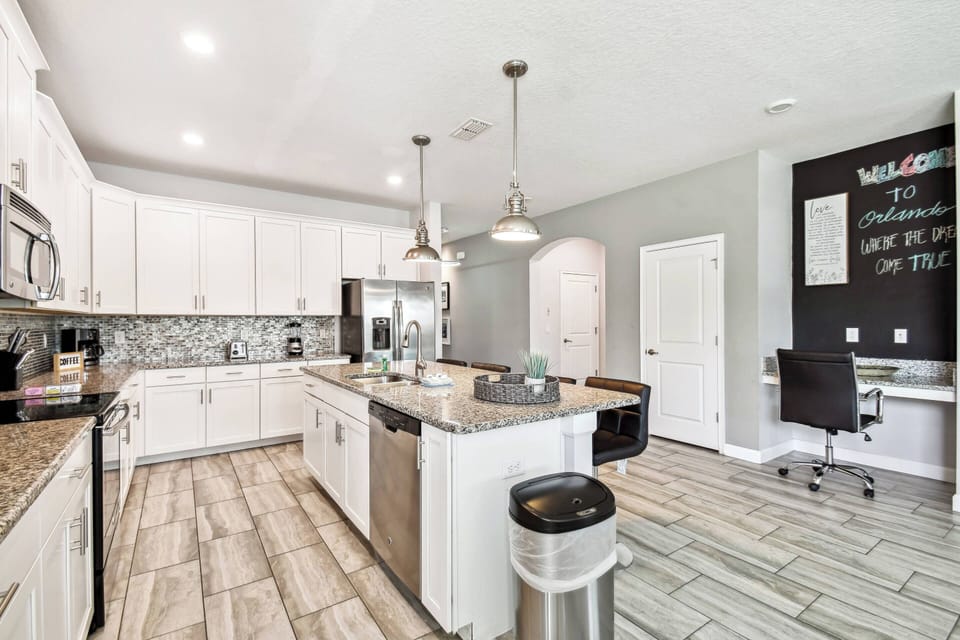 Enjoy culinary adventures in this spacious kitchen featuring sleek white cabinetry and a modern gray backsplash. The large island offers ample workspace, complemented by warm wood flooring for a cozy atmosphere.