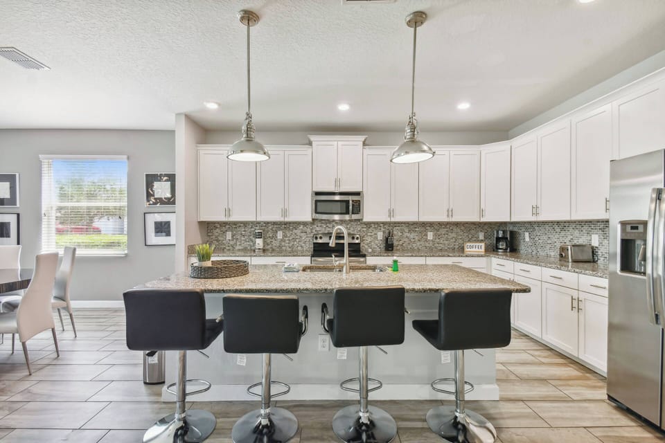 Experience a stylish kitchen with sleek white cabinetry and elegant stone countertops. Modern bar seating invites casual conversations, while large windows bathe the space in natural light, creating a cheerful atmosphere for.
