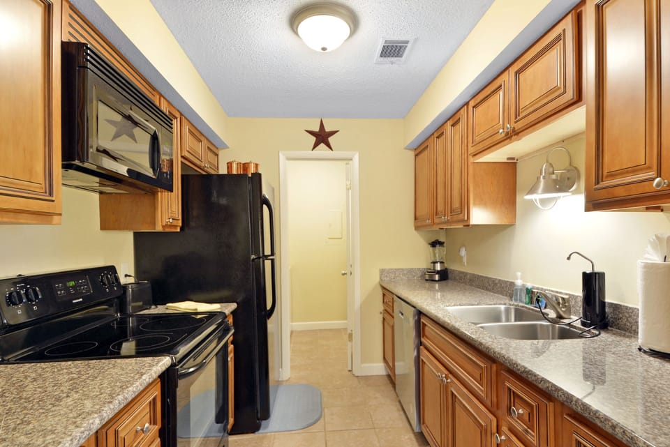 Galley Kitchen with Granite Counters - Kitchen with granite counters, black appliances, microwave, dishwasher, and full cooking setup.
