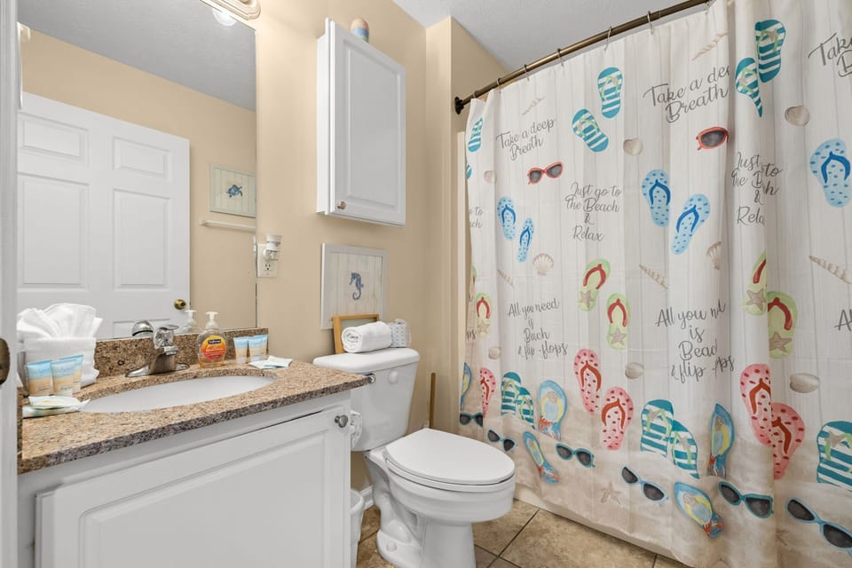Bathroom with a granite countertop and a colorful beach-themed shower curtain.