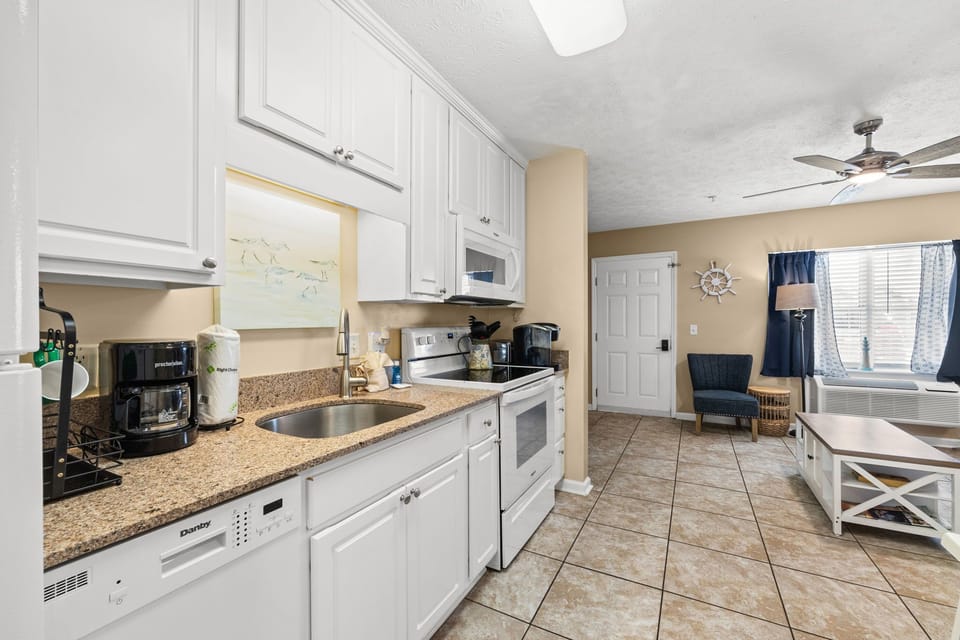 Modern kitchen with white cabinetry and granite countertops opening to a cozy living area.