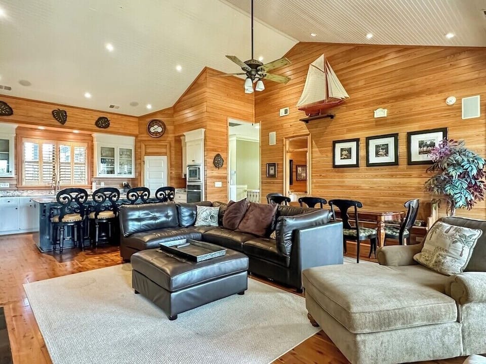 An open-concept family room and dining room with warm wood paneling, trim work, high ceilings, and a ceiling fan.
