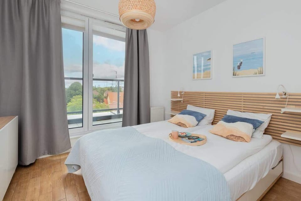 A bright bedroom featuring a comfortable double bed with light blue bedding and large windows.

