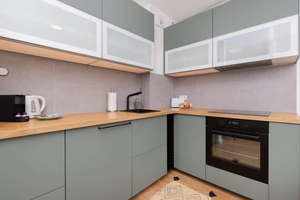 A contemporary kitchenette with sleek green cabinets, a built-in oven, and a minimalist design.

