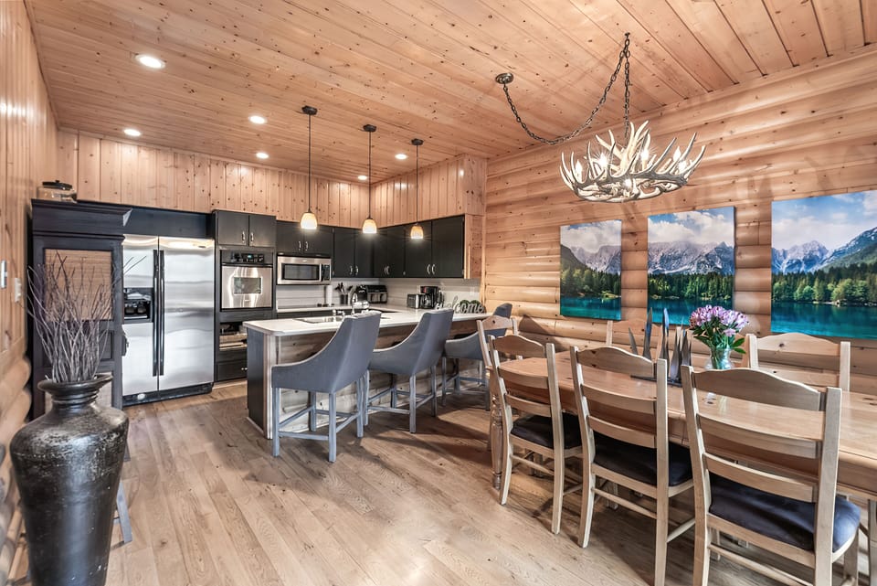 - Open kitchen with stainless steel appliances and wood cabinetry  
- Large dining table and breakfast bar with comfortable seating  
- Antler chandelier and scenic art create rustic mountain charm