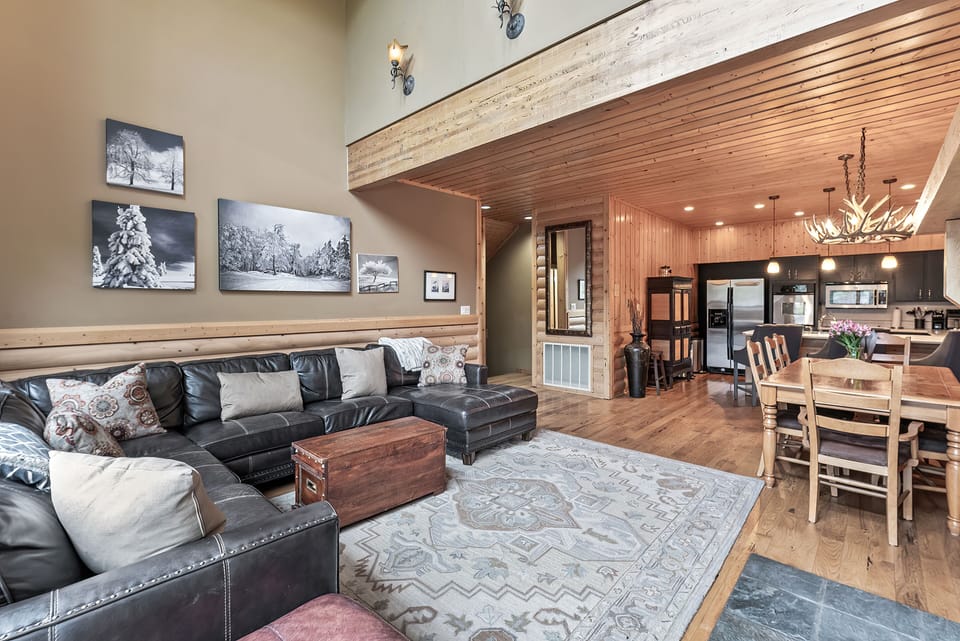 - Spacious open concept with wood floors and vaulted ceiling beams  
- Leather sectional seating with mountain-inspired wall decor  
- Easy flow to dining area and fully equipped modern kitchen