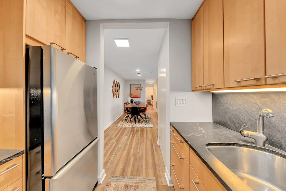 Kitchen entry view w/ stainless fridge, wood cabinetry & sightline to dining area