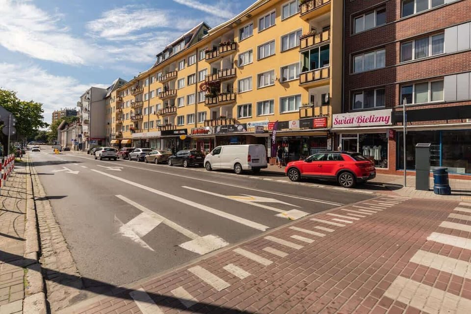 A bustling street with a mix of residential and commercial buildings, featuring wide sidewalks and pedestrian crossings.

