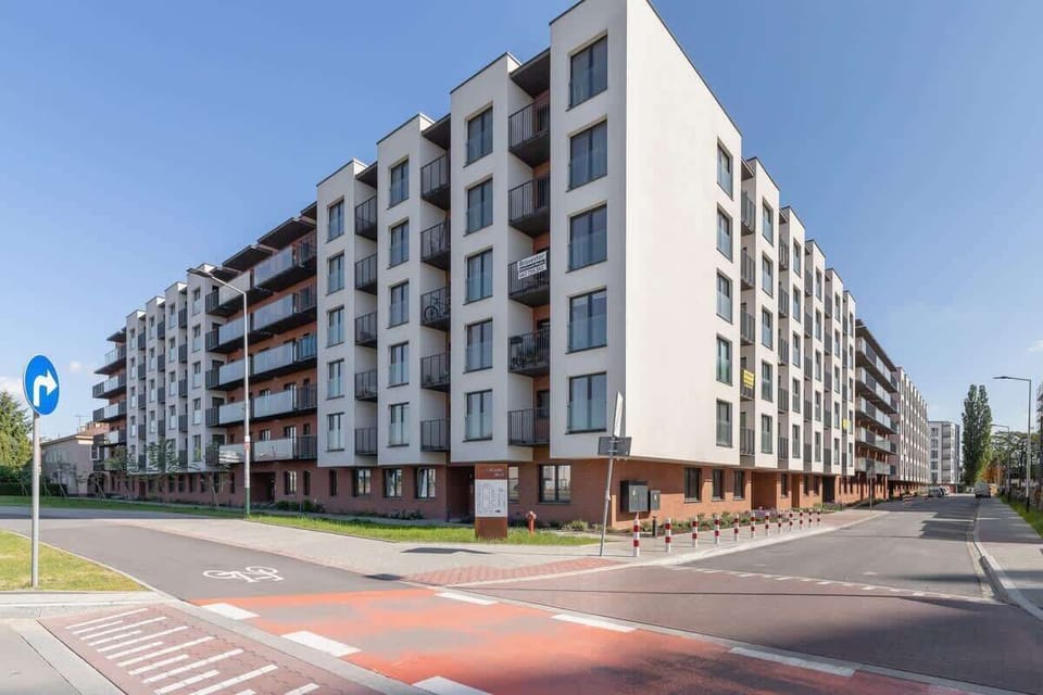 An exterior view of a modern apartment complex with clean lines, wide sidewalks, and a contemporary architectural design.

