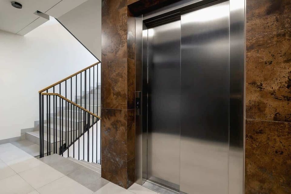 A clean and modern stairwell with a metallic elevator and well-lit interiors, ensuring convenience and accessibility.

