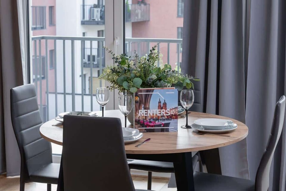 A dining area with a round table set for two, surrounded by large windows and curtains for a cozy atmosphere.

