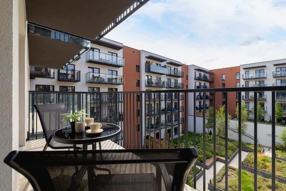 A balcony with a small table and chairs, overlooking a well-maintained courtyard, ideal for relaxing outdoors.

