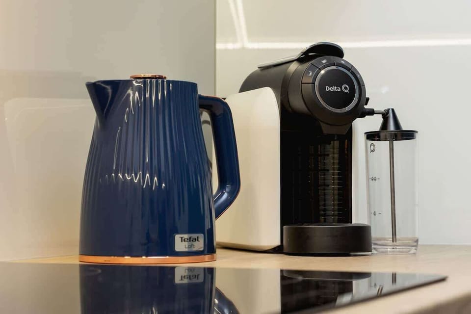 A close-up of a black capsule coffee machine and a blue ceramic pitcher, adding a touch of convenience and color to the kitchen countertop.
