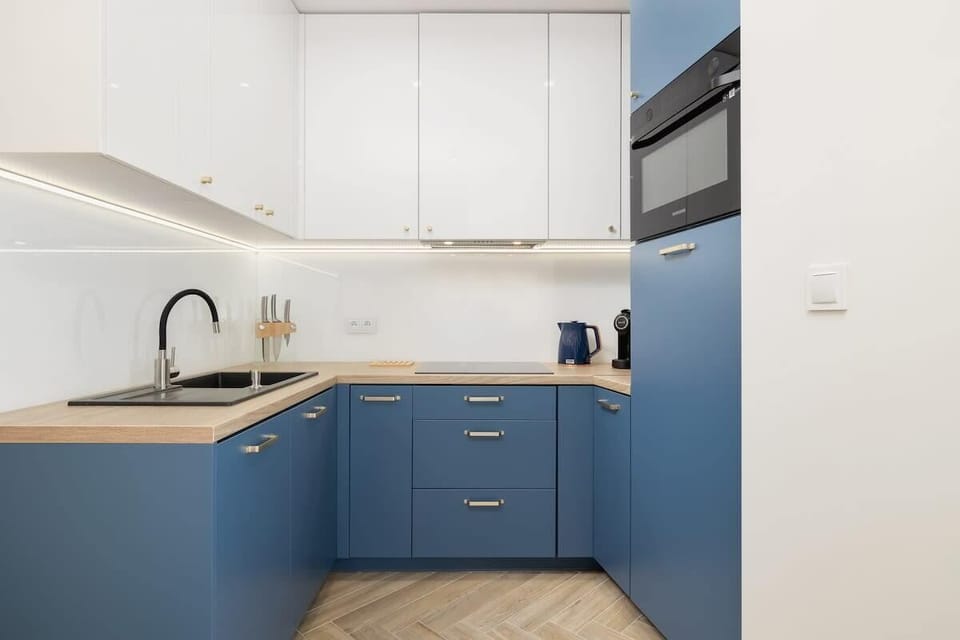 A sleek kitchen corner with white upper cabinets, blue lower cabinets, and a black faucet, offering a functional and contemporary cooking space.
