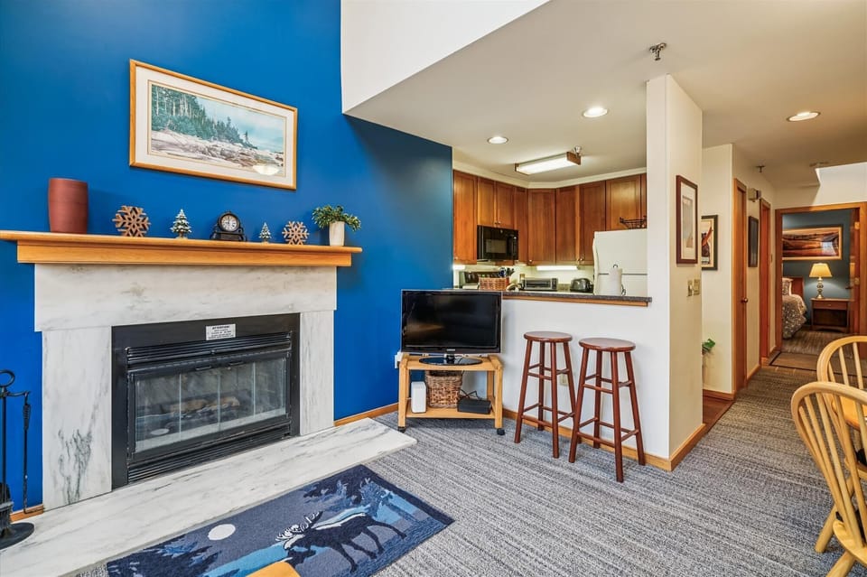 Open living space with a gas fireplace, breakfast bar seating for two, and a fully equipped kitchen just steps away.